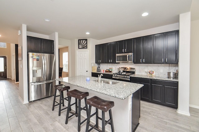 kitchen featuring a breakfast bar, sink, light stone counters, appliances with stainless steel finishes, and an island with sink