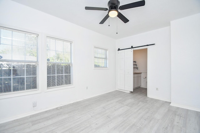 unfurnished bedroom featuring a barn door, light hardwood / wood-style floors, and ceiling fan