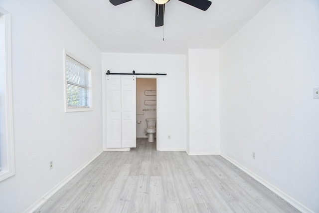 empty room featuring a barn door, ceiling fan, and light hardwood / wood-style flooring