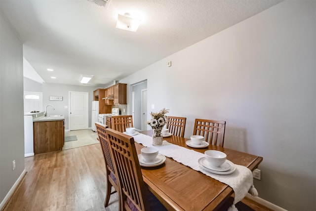 dining room featuring a textured ceiling, light wood-type flooring, lofted ceiling, and sink