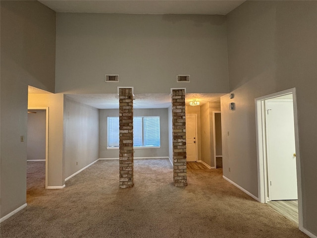 carpeted spare room featuring ornate columns and a high ceiling