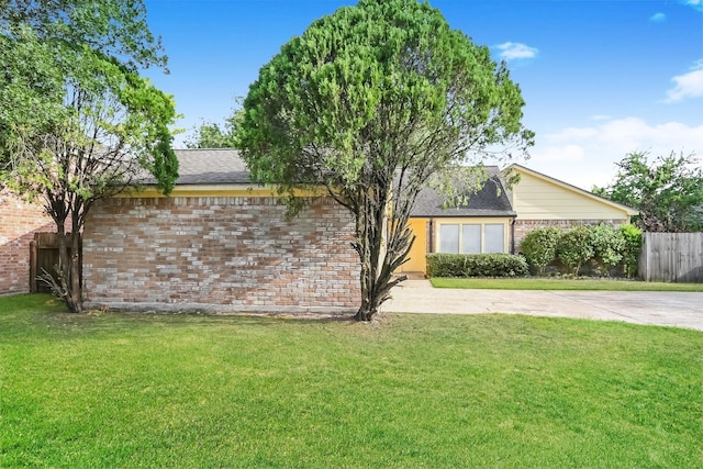 view of side of home featuring a shingled roof, brick siding, fence, and a lawn