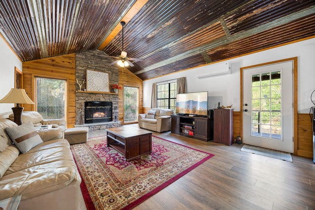 living room featuring wooden walls, ceiling fan, a fireplace, wood-type flooring, and a wall unit AC