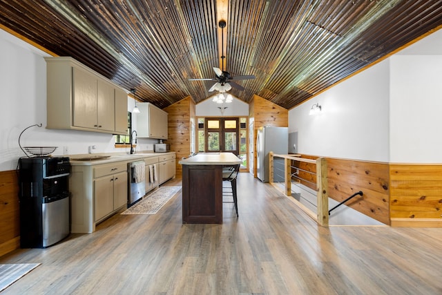 kitchen with stainless steel appliances, sink, hardwood / wood-style floors, a center island, and wood walls