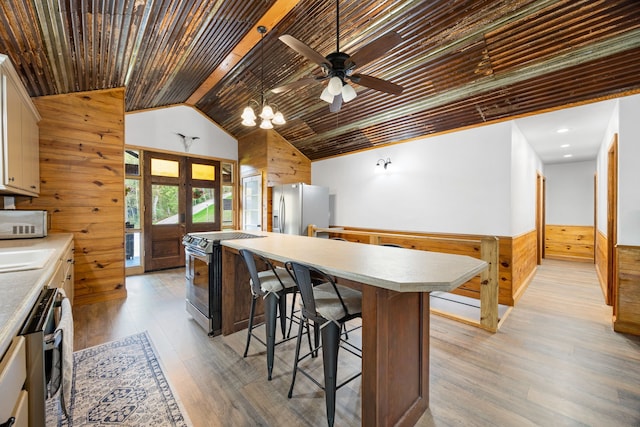 kitchen with wooden walls, light wood-type flooring, wood ceiling, and appliances with stainless steel finishes