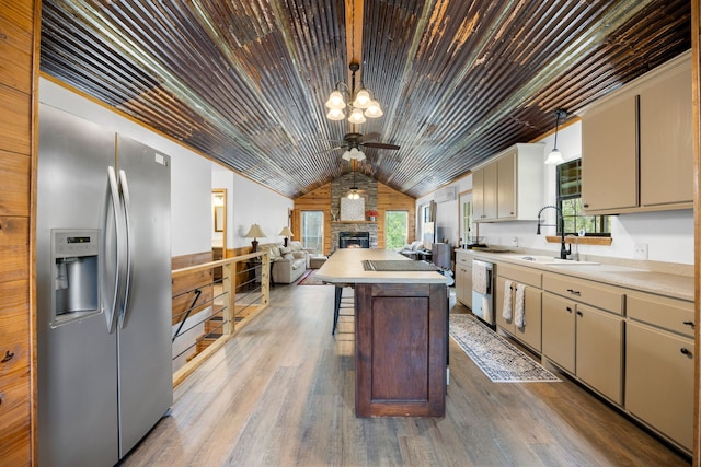 kitchen featuring a center island, cream cabinets, a stone fireplace, hanging light fixtures, and appliances with stainless steel finishes