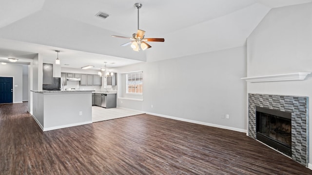 unfurnished living room featuring a tile fireplace, ceiling fan with notable chandelier, dark wood-type flooring, and vaulted ceiling