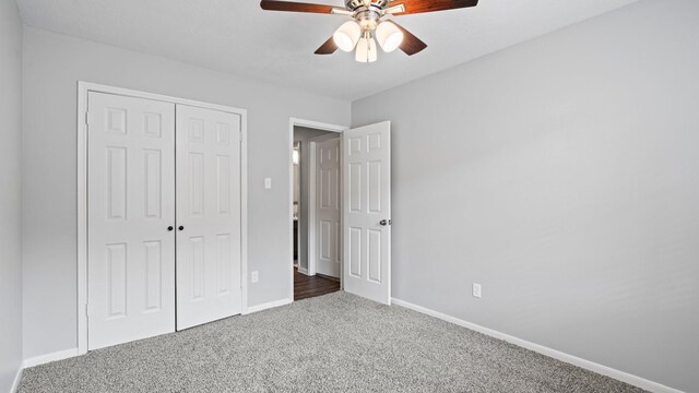 unfurnished bedroom featuring dark colored carpet, a closet, and ceiling fan