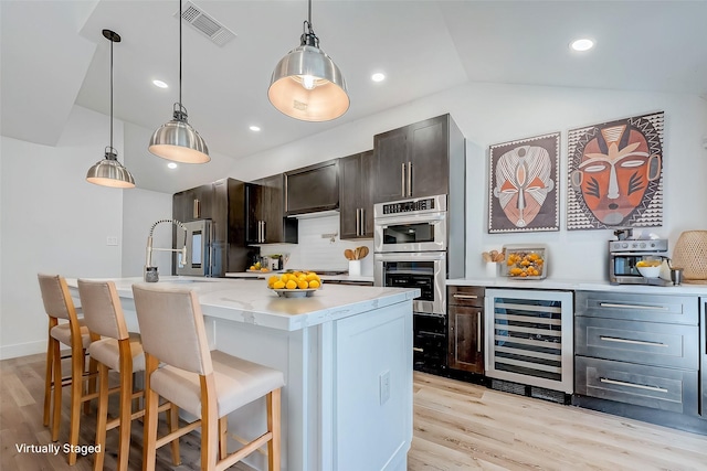 kitchen featuring lofted ceiling, a kitchen island with sink, hanging light fixtures, wine cooler, and light hardwood / wood-style floors