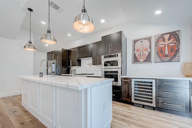 kitchen featuring hanging light fixtures, beverage cooler, light hardwood / wood-style floors, lofted ceiling, and a center island with sink