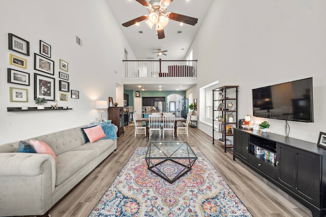 living room with ceiling fan, light wood-type flooring, and high vaulted ceiling