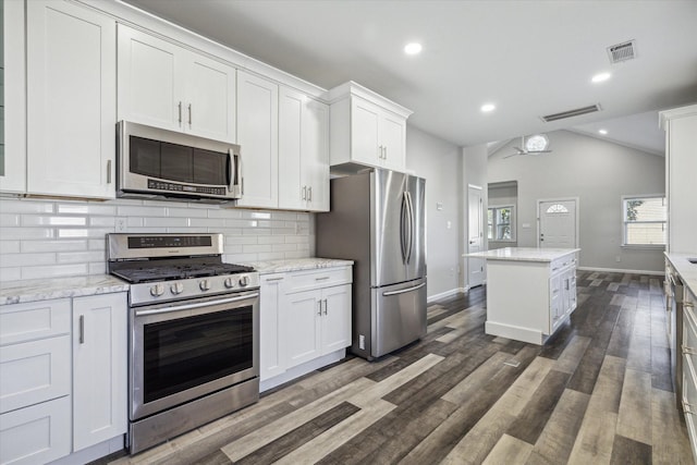 kitchen with dark wood-type flooring, white cabinets, vaulted ceiling, appliances with stainless steel finishes, and light stone counters