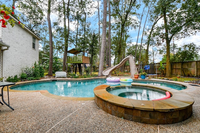 view of pool featuring a water slide and an in ground hot tub