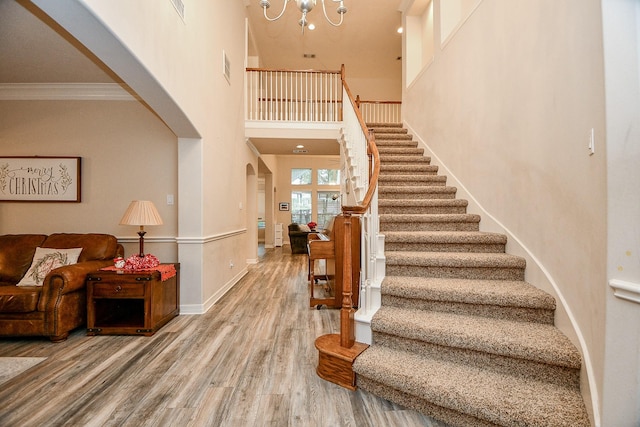 stairs featuring a chandelier, wood-type flooring, crown molding, and a high ceiling