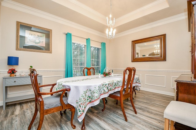 dining area with a raised ceiling, wood-type flooring, crown molding, and a chandelier