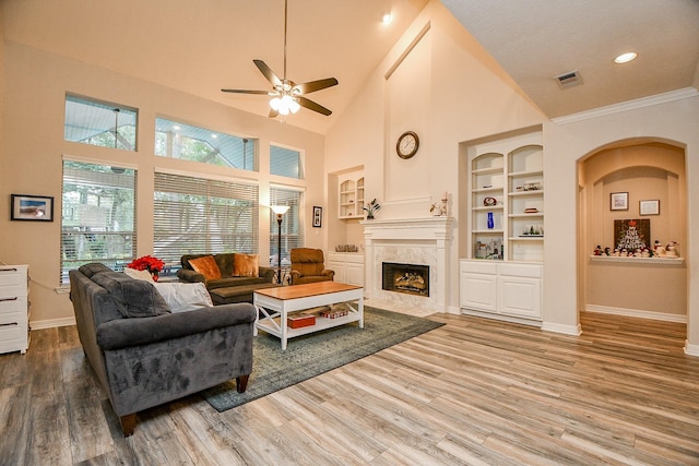 living room with built in shelves, ceiling fan, wood-type flooring, high vaulted ceiling, and a premium fireplace