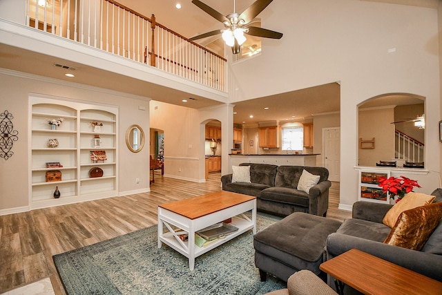 living room featuring high vaulted ceiling, crown molding, ceiling fan, built in features, and light wood-type flooring