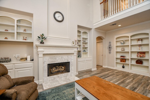 living room featuring a high end fireplace, ornamental molding, a high ceiling, built in shelves, and hardwood / wood-style floors