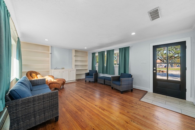 living room with wood-type flooring, built in shelves, and ornamental molding