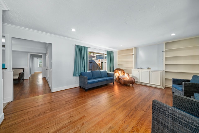 living area featuring hardwood / wood-style flooring, built in shelves, ornamental molding, and a textured ceiling