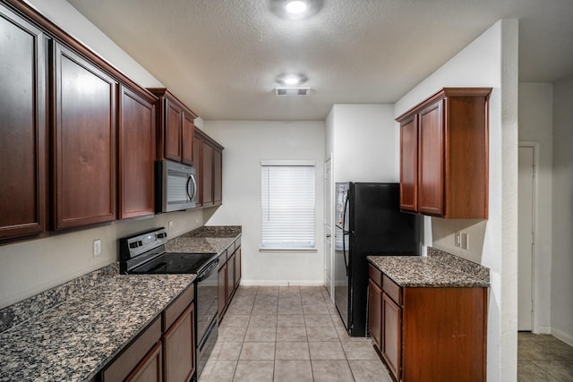 kitchen with light tile patterned floors, a textured ceiling, dark stone counters, and black appliances