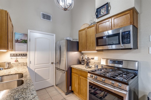 kitchen featuring sink, light stone counters, a chandelier, light tile patterned floors, and appliances with stainless steel finishes