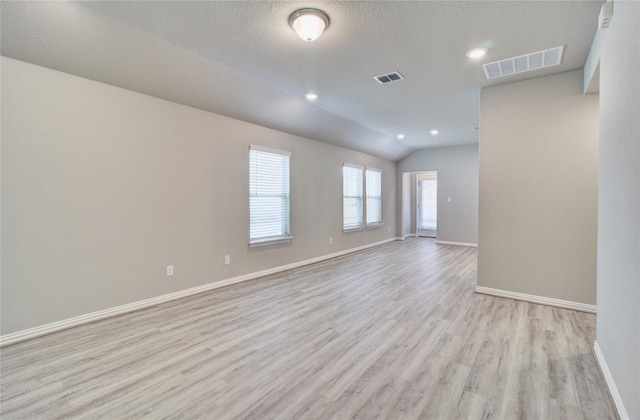 spare room featuring lofted ceiling, a textured ceiling, and light hardwood / wood-style flooring