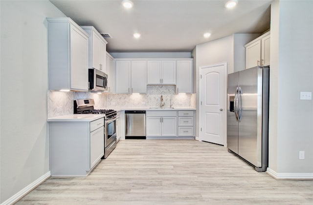 kitchen featuring backsplash, white cabinets, sink, light hardwood / wood-style flooring, and appliances with stainless steel finishes