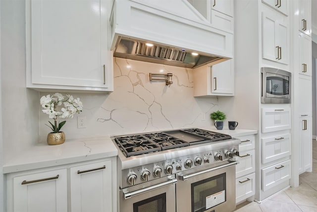 kitchen featuring appliances with stainless steel finishes, white cabinetry, decorative backsplash, light stone countertops, and custom range hood