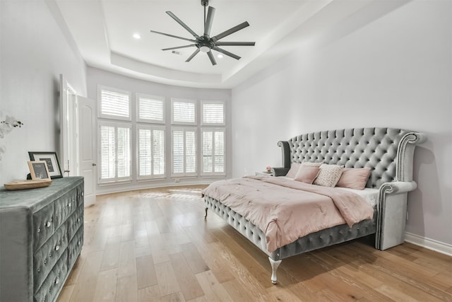 bedroom with a tray ceiling, ceiling fan, and light wood-type flooring