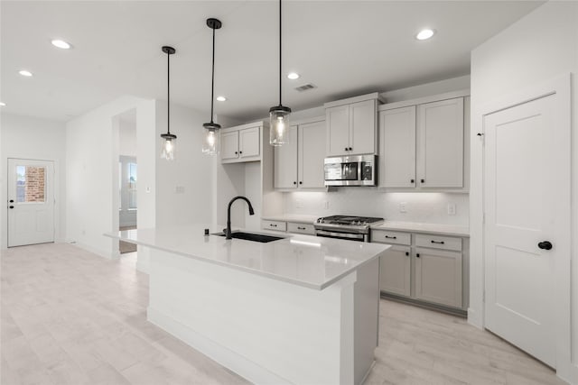 kitchen with appliances with stainless steel finishes, a center island with sink, hanging light fixtures, and sink