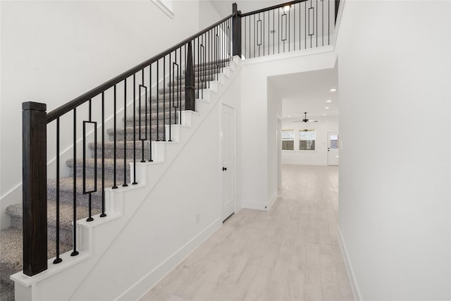 staircase featuring hardwood / wood-style flooring, ceiling fan, and a towering ceiling