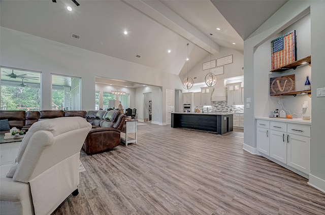 living room featuring beam ceiling, ceiling fan with notable chandelier, light hardwood / wood-style floors, and high vaulted ceiling