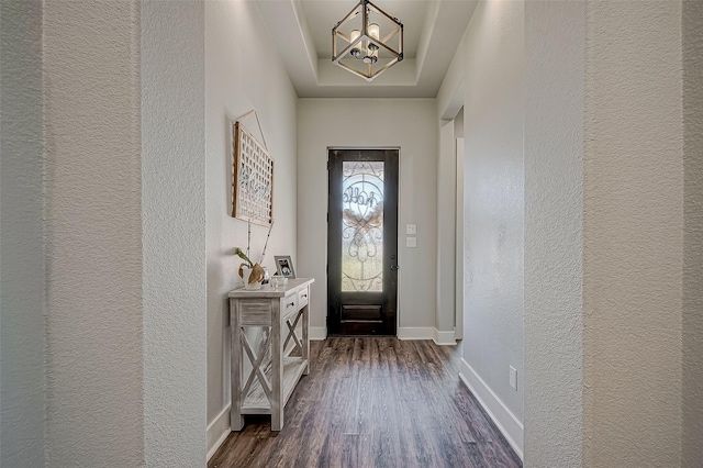 entryway featuring dark hardwood / wood-style floors, a raised ceiling, and an inviting chandelier