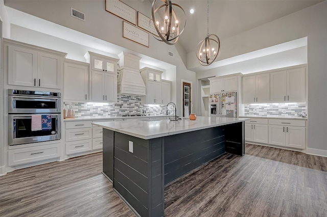 kitchen featuring high vaulted ceiling, a center island with sink, decorative light fixtures, a notable chandelier, and stainless steel appliances