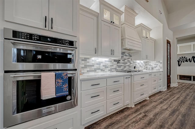 kitchen with custom exhaust hood, backsplash, dark hardwood / wood-style flooring, white cabinetry, and stainless steel appliances