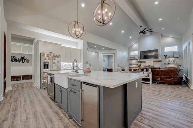 kitchen with gray cabinetry, ceiling fan with notable chandelier, pendant lighting, a center island with sink, and high vaulted ceiling