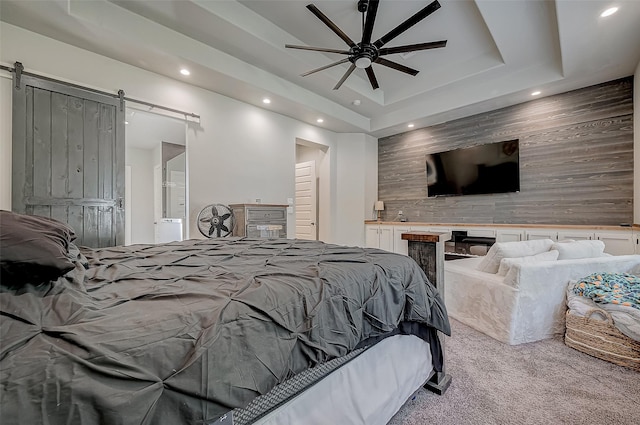 bedroom featuring ceiling fan, a barn door, light carpet, and a tray ceiling