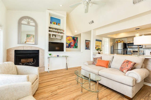 living room featuring a tile fireplace, light hardwood / wood-style floors, and ceiling fan