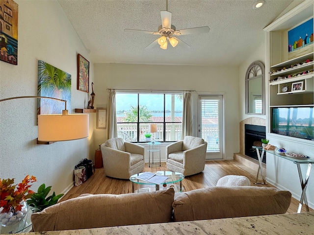 living room with ceiling fan, light wood-type flooring, a textured ceiling, and lofted ceiling