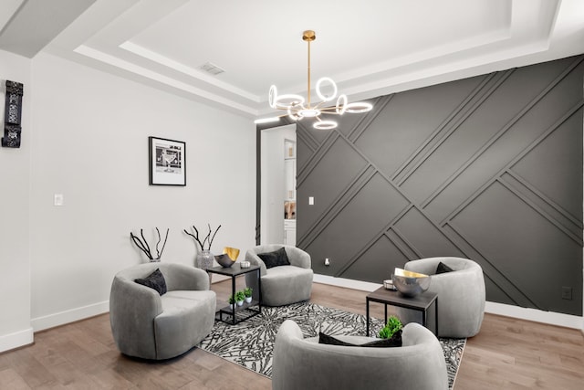 sitting room with a chandelier, light hardwood / wood-style flooring, and a tray ceiling