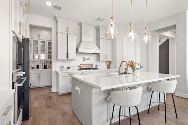 kitchen featuring white cabinets, light hardwood / wood-style floors, premium range hood, and a kitchen island with sink