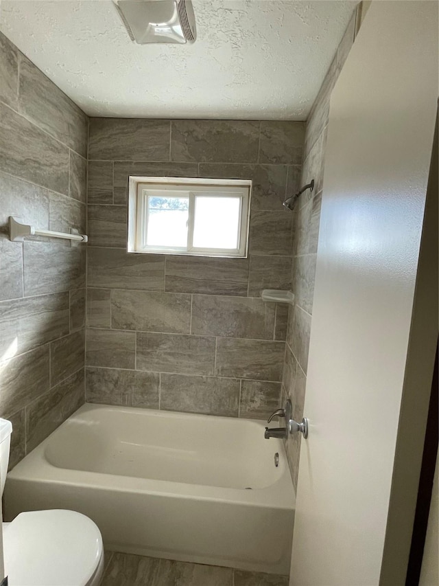 bathroom featuring tiled shower / bath, a textured ceiling, and toilet