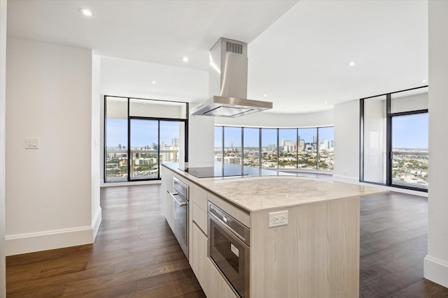 kitchen featuring black electric cooktop, wall chimney exhaust hood, a healthy amount of sunlight, and a kitchen island