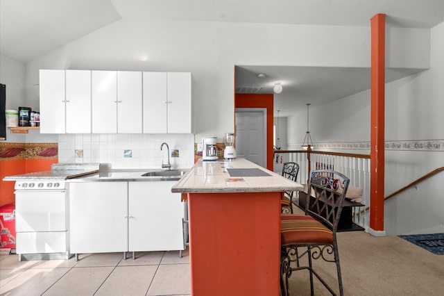 kitchen featuring white cabinets, sink, vaulted ceiling, light colored carpet, and a breakfast bar area