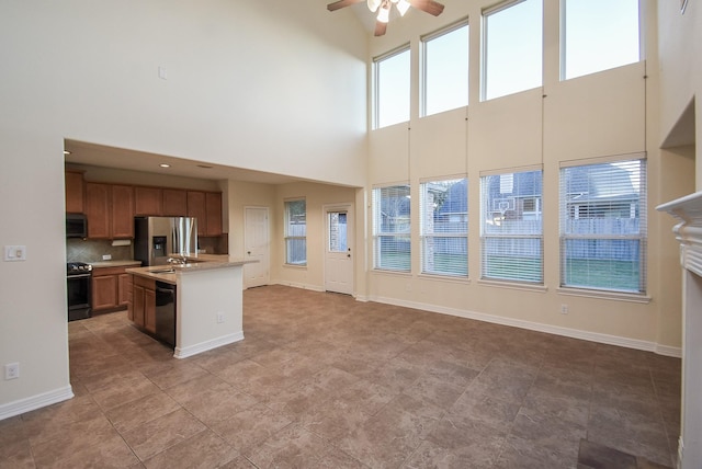 kitchen featuring a towering ceiling, backsplash, ceiling fan, black appliances, and a center island with sink