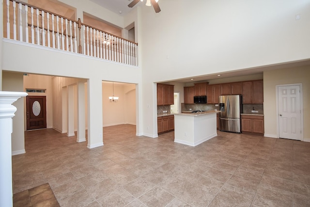 kitchen with decorative backsplash, stainless steel refrigerator with ice dispenser, a towering ceiling, ceiling fan with notable chandelier, and hanging light fixtures