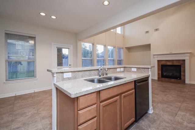 kitchen with a tile fireplace, sink, black dishwasher, light stone counters, and a kitchen island with sink