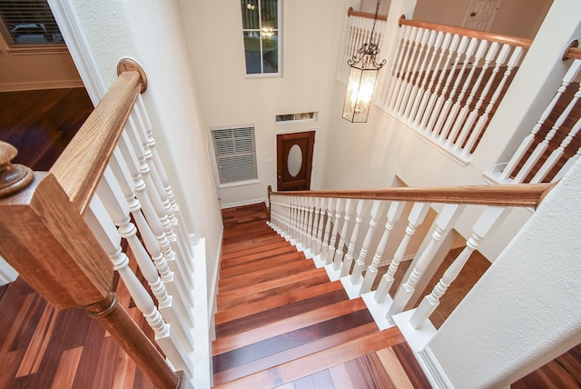 staircase with wood-type flooring, a notable chandelier, and a high ceiling