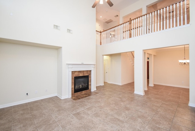 unfurnished living room with ceiling fan with notable chandelier, a tile fireplace, and a high ceiling